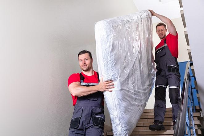 two people carrying a box spring out of a room in Hauppauge